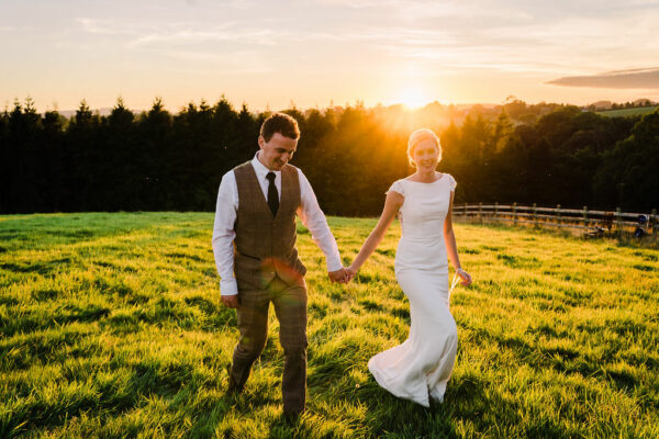 Bride and Groom Walk Through Field Hand in Hand - Intimate Wedding - Cumbria Tipi Wedding