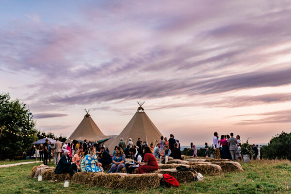 Lake District Tipi Wedding - beautiful pastel sunset behind the tipis with lots of guests on haybales - Authentic Tentipi Tipis