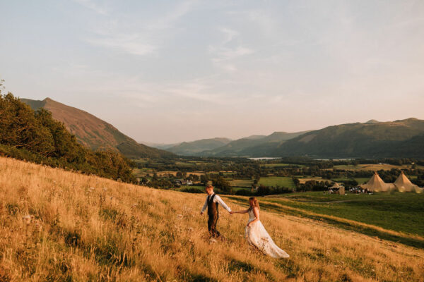 Lake District wedding - couple running up a hill with the Lake District Mountains in the back ground. Autumn wedding